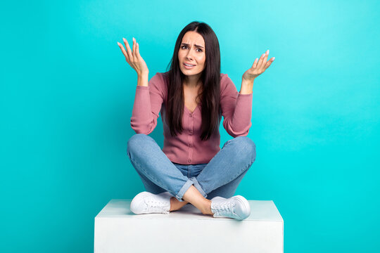Full body length photo of hesitant lady shrug shoulders unhappy questioned what happened sit white platform isolated on cyan color background