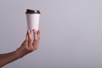 Man hand holding a hot Coffee paper cup isolated on grey background. Male hand holds a disposable mug with a black lid. Empty space coffee cup and background.