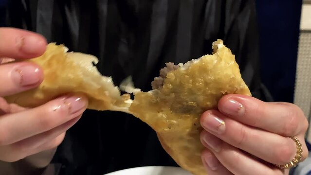 Unrecognizable woman tearing oiled pastry Uzbek cheburek in half