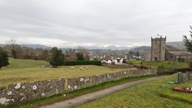 St Michael and All Angels Church in Hawkshead, showing fields and grazing sheep Cumbria, UK