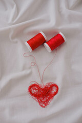 Red thread and heart on white fabric. Valentine's day concept.