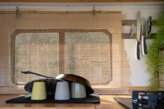 clean dishes and frying pan draining in the kitchen of a camper van, window with bamboo curtain giving a natural and warm lighting inside the van.