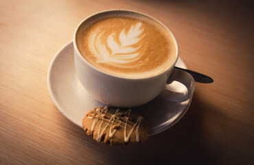 A refreshing coffee with artwork in foam along with a cookie