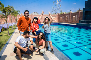 Group of young indian friends having fun standing at pool side resort in hot sunny day. Summer...