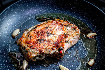 Grilled premium rib eye beef steak in the pan, cooking steak in the kitchen on a dark background. Overhead shot of chef preparing ribeye with butter, thyme and garlic.
