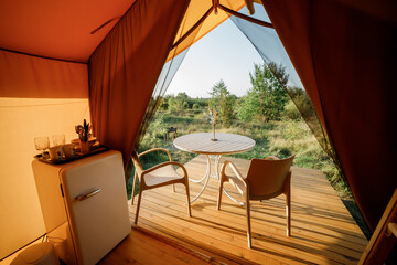 Interior of Cozy open glamping tent with light inside during sunset. Luxury camping tent for outdoor summer holiday and vacation. Lifestyle concept - 584702031