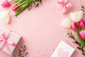 Mother's Day concept. Top view photo of gift boxes with bows bouquets of tulips envelope with postcard and sprinkles on isolated pastel pink background with blank space in the middle