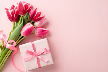 Mother's Day celebration concept. Top view photo of giftbox with ribbon bow and bouquet of pink tulips on isolated pastel pink background with copyspace