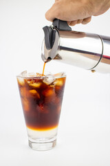 Barista pouring coffee into a glass  with ice cubes on white background