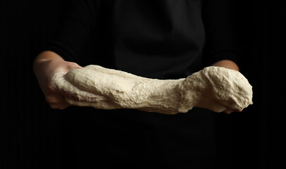 Fresh sourdough dough in the hands of the chef on a black background.