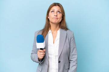 Fototapeta premium Middle-aged TV presenter woman over isolated blue background and looking up
