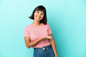 Young mixed race woman isolated on blue background presenting an idea while looking smiling towards