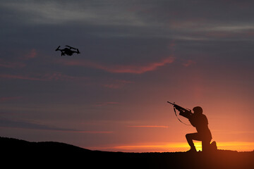 Fototapeta na wymiar Soldier trying to shoot down reconnaissance drone against the backdrop of a sunset.
