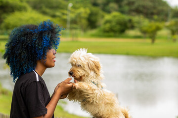 Uma jovem negra de cabelos tingidos de azul, segurando as patas dianteiras de seu cachorro que...