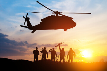 Silhouettes of helicopter and soldiers on background of sunset.