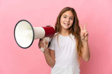 Child over isolated pink background holding a megaphone and smiling and showing victory sign