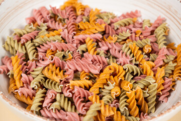 Rice vegetable pasta in the form of spirals in a bowl. Healthy rice pasta with tomatoes, selenera, carrots and beets