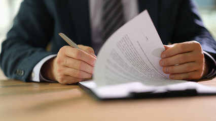 Businessman leafing through documents and signing contract for business deal at work in office closeup
