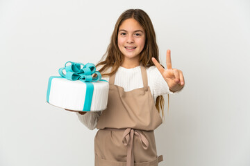 Little girl holding a big cake over isolated white background smiling and showing victory sign