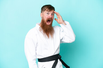 Redhead man with long beard doing karate isolated on blue background doing surprise gesture while looking to the side