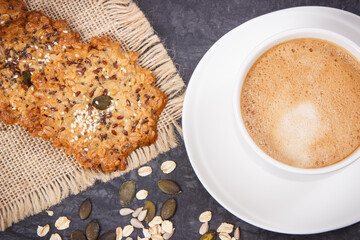 Cup of coffee with milk and fresh baked oatmeal cookies with honey and healthy seeds. Delicious crunchy dessert