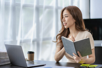 Asian female financial analyst or accountant using laptop in accounting firm working on financial...