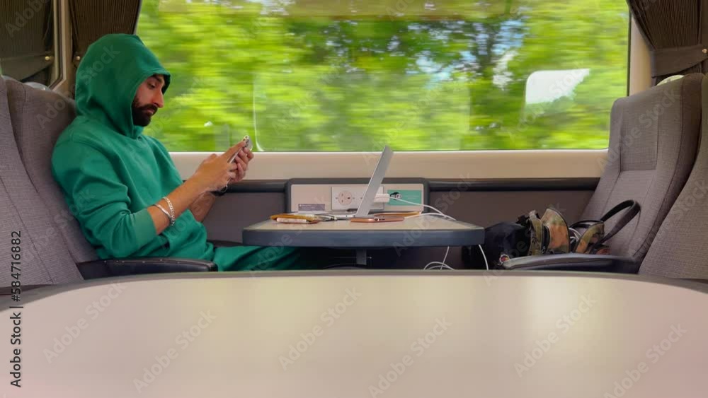 Poster man in hoodie using mobile phone while traveling on train with laptop on table. - slow motion