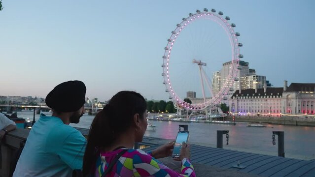 Young Punjabi Man And Indian Woman With London Eye In The Background On The South Bank Of River Thames in London. - medium
