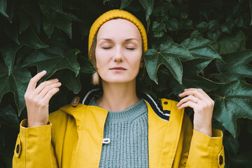 Portrait of relaxed and confident woman with eyes closed on background of green leaves wall....