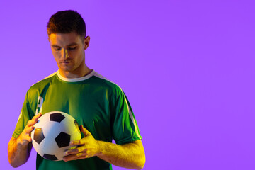 Caucasian male soccer player with football over neon pink lighting