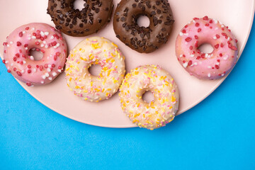 Many different donuts on a blue background top view, pink, white and chocolate donuts