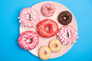 Many different donuts on a blue background top view, pink, white and chocolate donuts