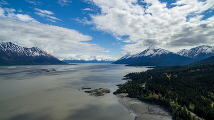 Aerial view of a snowy mountain range covered with clouds against a lake in Hope, Alaska