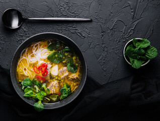 Chicken soup with vegetables in black bowl with red pepper