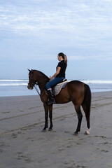 Young woman riding a horse on the beach at the ocean.
