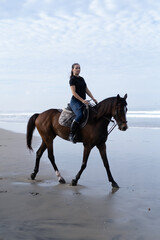 Young woman riding a horse on the beach at the ocean.