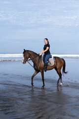 Fototapeta na wymiar Young woman riding a horse on the beach at the ocean.