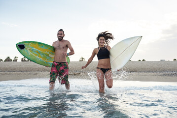Cheerful couple running in water with surfboards.