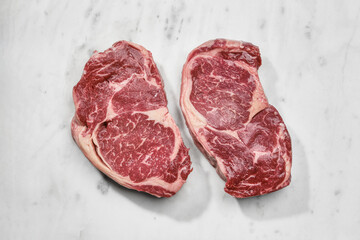 Two slices of raw beef fillet steaks on white marble background, top view. 