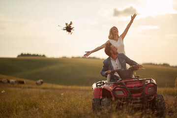 Attractive newlyweds driving quad together; Rural wedding concept