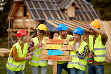 A group of young cheerful both female and male builders enjoy posing for a photo at a cottage...