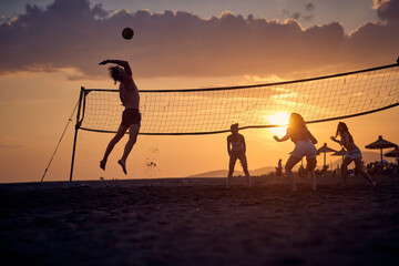 A group of friends is playing the volleyball on the beach while sun is setting. Sport, sea, beach