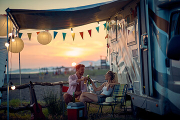 Couple toasting with beer sitting in front of camper. Travel, holiday, weekend, togetherness, lifestyle concept.