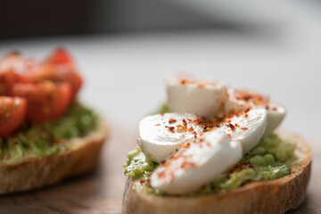 Bruschettas with avocado, tomato and mozzarella on wood board on concrete bacground