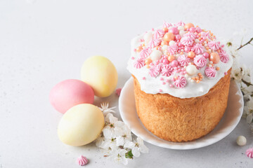 Traditional Easter sweet bread or cakes with white icing and sugar decor, colored eggs and cherry blossom tree branch over white table. Various Spring Easter cakes. Happy Easter day. Selective focus.
