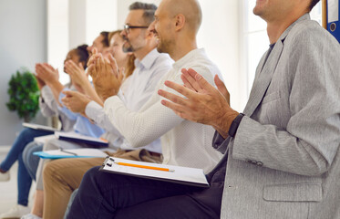 Business audience applauding. Happy people with clipboards and pencils sitting in row at business conference and clapping hands for professional speaker after interesting workshop and presentation