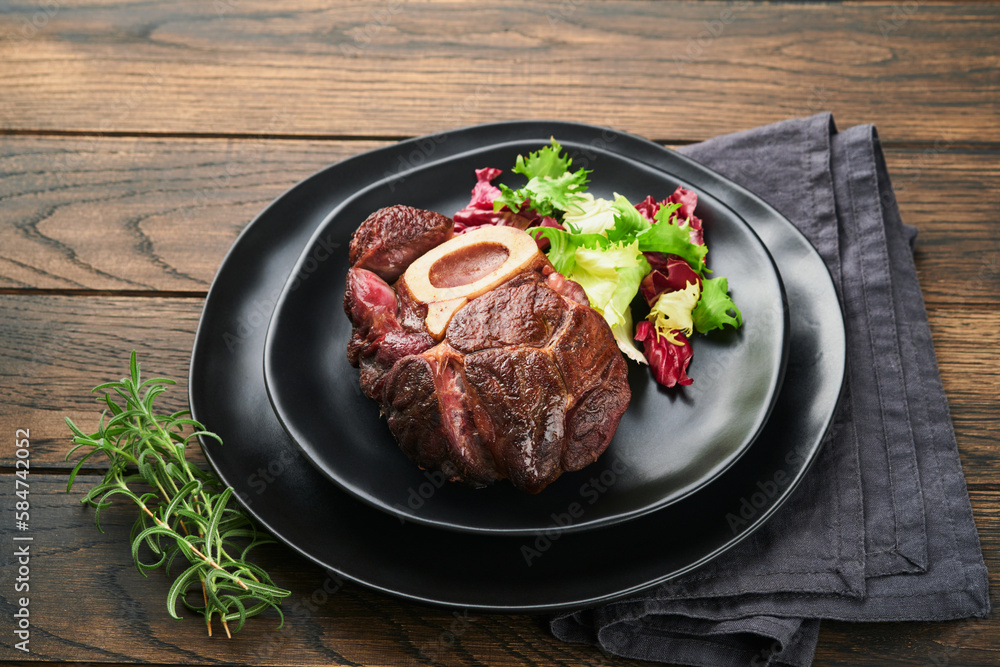 Wall mural Steaks Osso Buco. Sliced beef grilled Osso Buco or porterhouse meat steak with garnished with salad and french fries on black marble board on old wooden background. Top view. Mock up.