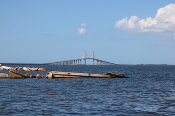 Obraz premium A broken jetty just before the Sunshine Skyway Bridge to St. Petersburg Florida. the jetty and pier are in focus with the bridge in the background. Deep blue Tampa bay water and blue sky with clouds