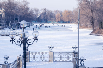 people are skating in the city winter park against the backdrop of trees, ice figures, a street...