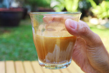 Closeup of Hand Holding a Glass of Dirty Latte Coffee